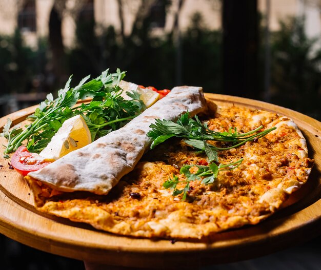 Side view lahmajun with ground meat greens and lemons on a tray