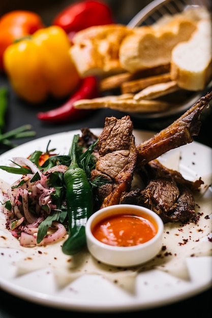 Foto gratuita vista laterale del kebab delle costole dell'agnello con le erbe verdi del peperoncino e la salsa piccante su un piatto bianco