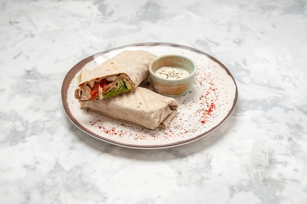 Side view of lavash wrap and yogurt in a small bowl on a plate on stained white surface