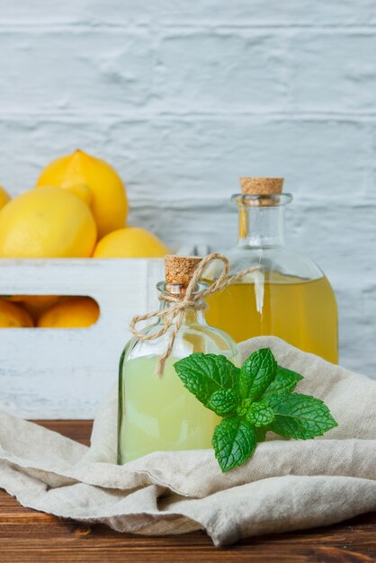 Вид сбоку лимонный сок с лимонами на деревянном ящике на деревянной и белой поверхности. вертикальное пространство для текста