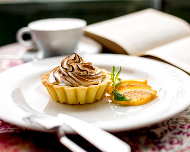 Side view of lemon tartlet with meringue decorated with lemon slices on a plate