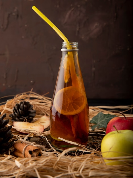 Бесплатное фото Вид сбоку лимонный чай с лаймом, корицей, плющом листьев, шишка, красные и зеленые яблоки на соломе