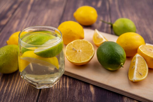 Side view lemons with limes on a cutting board with a glass of detox water on a wooden background