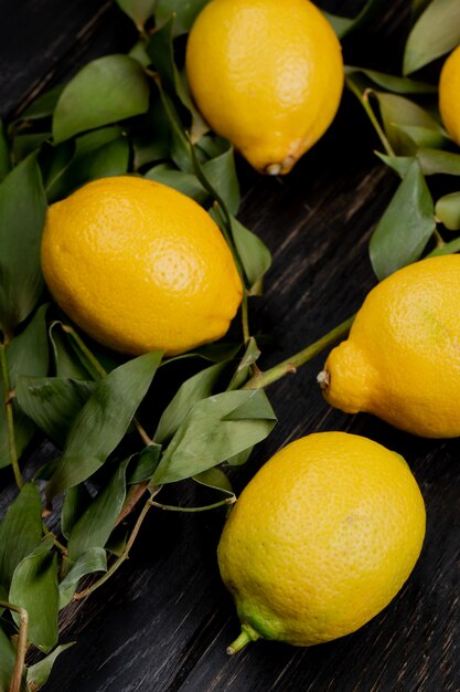 Side view of lemons on wooden background decorated with leaves