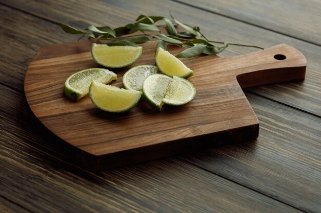 Side view of lime slices with leaves on cutting board on wooden background