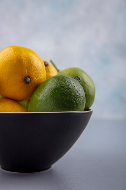 Side view limes and lemons in a black bowl on a gray background