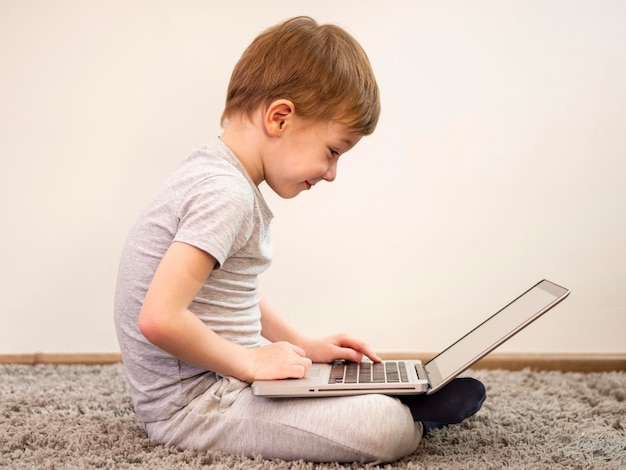 Foto gratuita ragazzino di vista laterale che gioca sul suo computer portatile