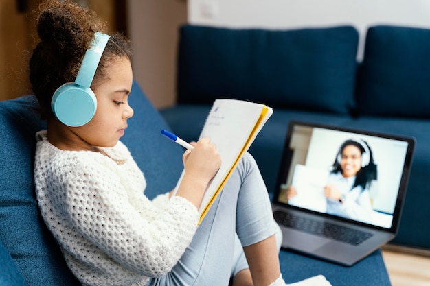 Side view of little girl during online school with laptop and headphones