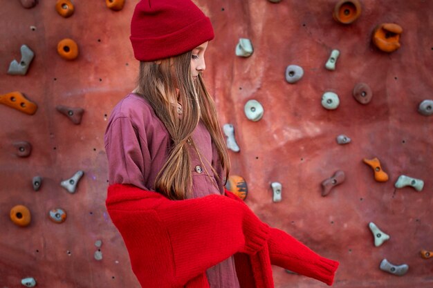 Side view little girl standing next to a climbing wall