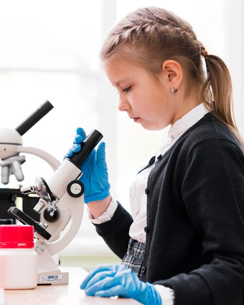 Вид сбоку маленькая девочка с микроскопом