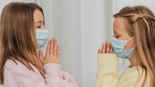 Side view of little girls praying with medical masks