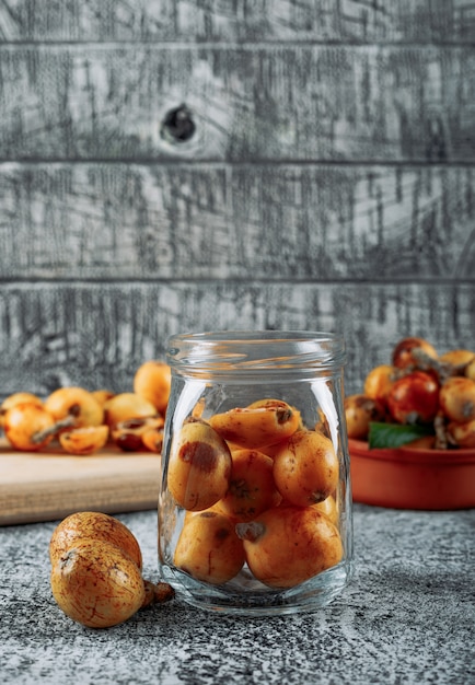 Free photo side view loquats in jar on gray textured background. vertical, space for text