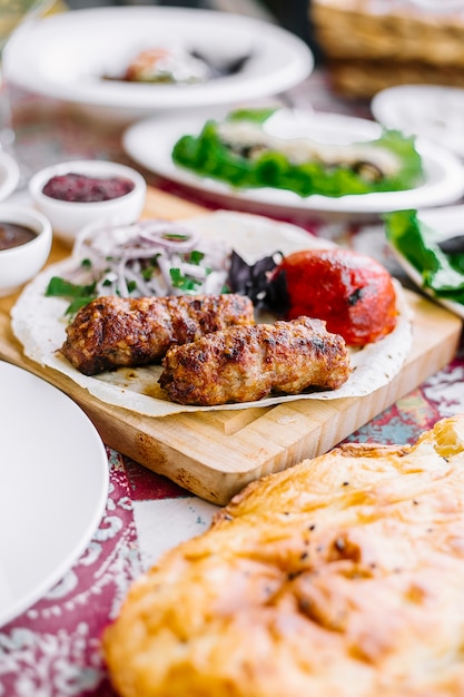 Side view of lula kebab on lavash with grilled tomato fresh herbs onion and spicies on a wooden board