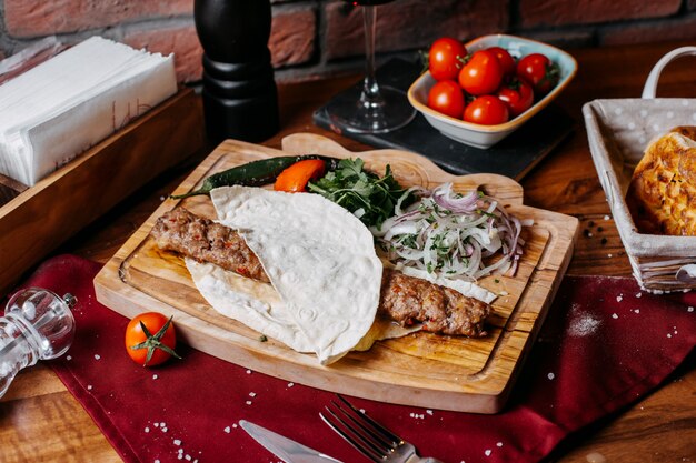 Side view of lula kebab with onions herbs and vegetables on a wooden board