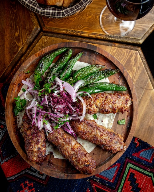 Side view of lula kebab with red onions  sumakh and grilled green chili peppers on a wooden board on the tablejpg