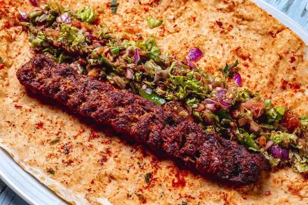 Side view lulya kebab with red onion geens hot green pepper salt and pepper on pita