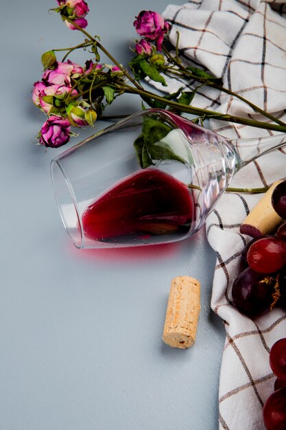 Side view of lying glass of red wine with flowers and corks on cloth on white