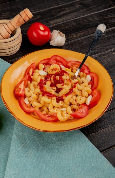 Side view of macaroni pasta in plate with garlic tomato garlic on blue cloth and wooden table