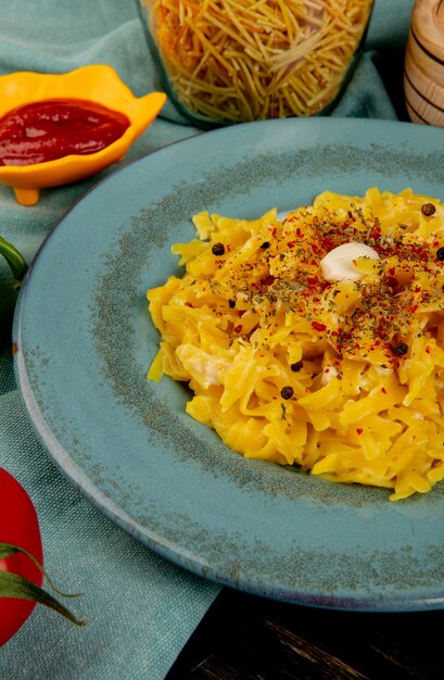 Side view of macaroni pasta in plate with ketchup spaghetti tomato on blue cloth and wooden table