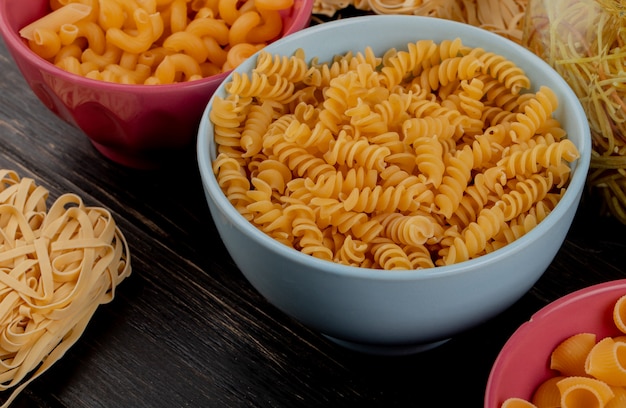 Side view of macaronis as rotini tagliatelle cavatappi pipe-rigate and others on wooden table