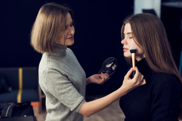 Side view makeup artist applying powder on model