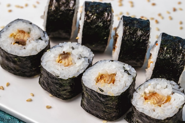 Riso maki vista laterale avvolto in alghe con pesce fritto e semi di sesamo sul tavolo