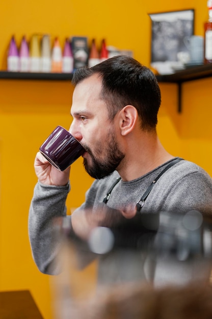 Вид сбоку мужского бариста, пьющего кофе