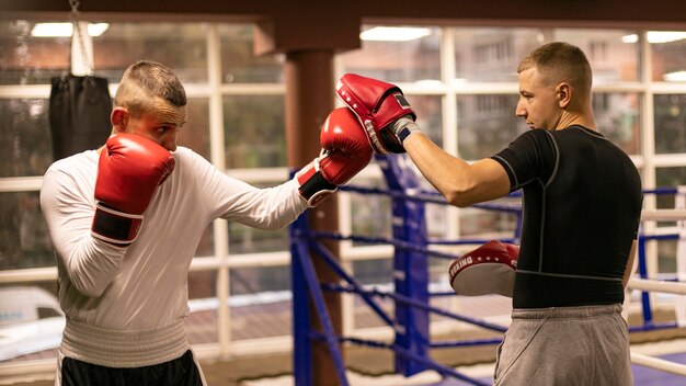 Боксер-мужчина тренируется с тренером рядом с рингом, вид сбоку