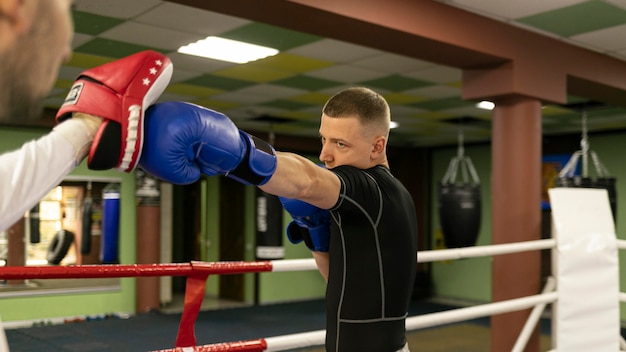 Вид сбоку на боксера-мужчину в перчатках, тренирующегося с тренером