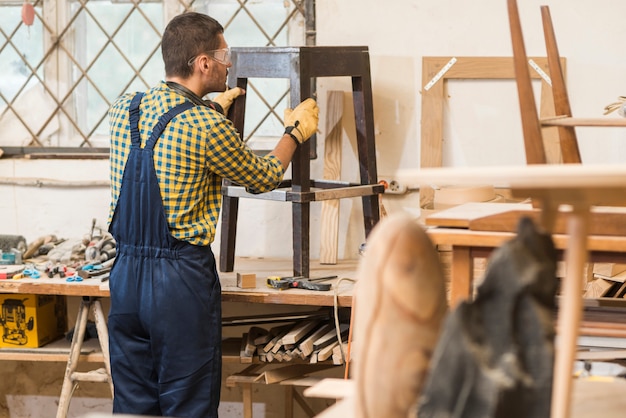 Вид сбоку мужского плотника, делая деревянную мебель в мастерской