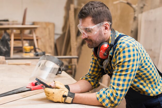 Вид сбоку мужского плотника с помощью мобильного телефона в мастерской