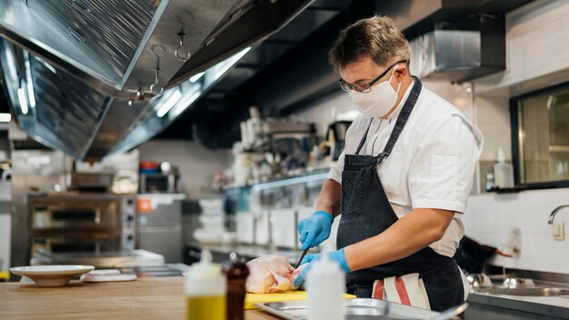 Side view of male chef with mask cutting chicken