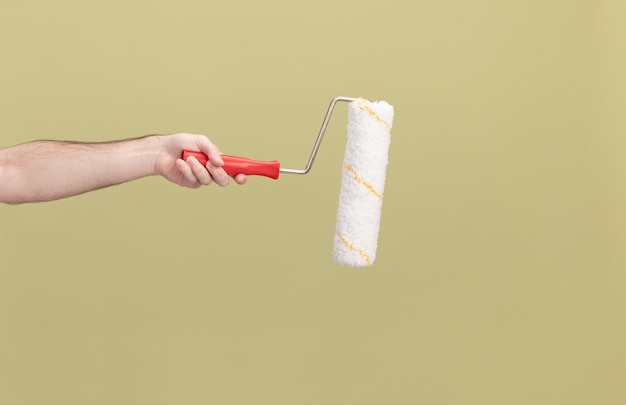 Side view of male hand with paint roller over green isolated wall