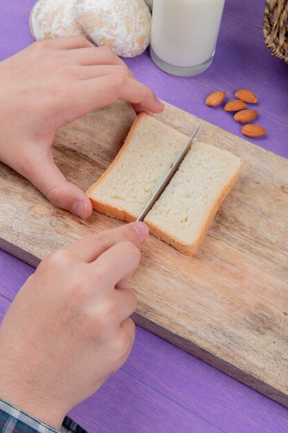 보라색 표면에 아몬드 gingerbreads 우유와 함께 보드 절단에 빵 조각을 절단 남성 손의 측면보기