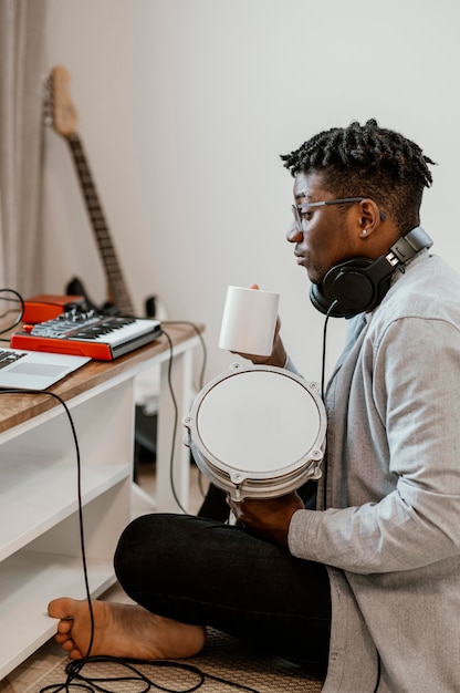 Free photo side view of male musician at home playing drums and mixing with laptop