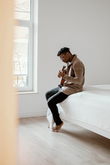 Side view of male musician playing guitar on bed