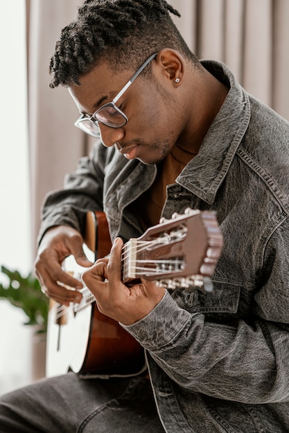 Side view of male musician playing guitar at home