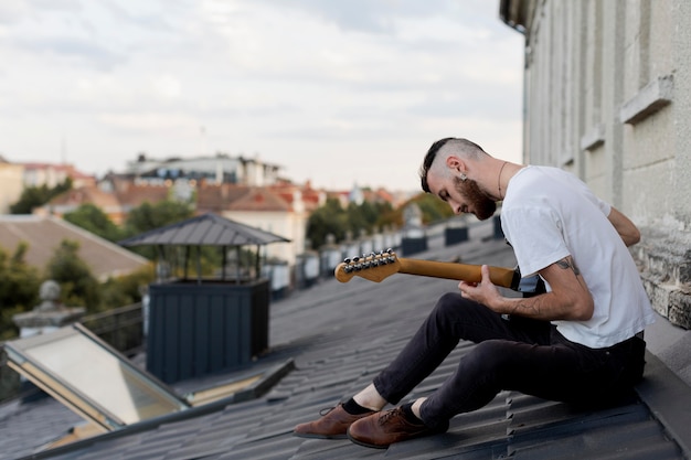 Side view of male musician on roof top playing electric guitar