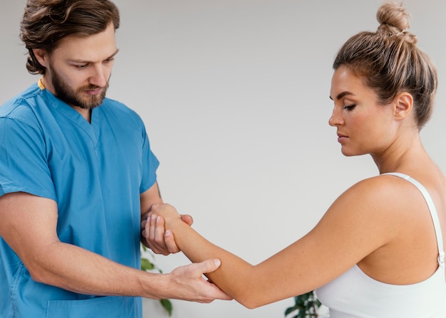 Side view of male osteopathic therapist checking female patient's elbow movement