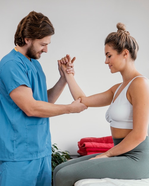 Side view of male osteopathic therapist checking female patient's elbow