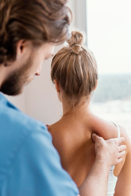 Side view of male osteopathic therapist checking female patient's spine