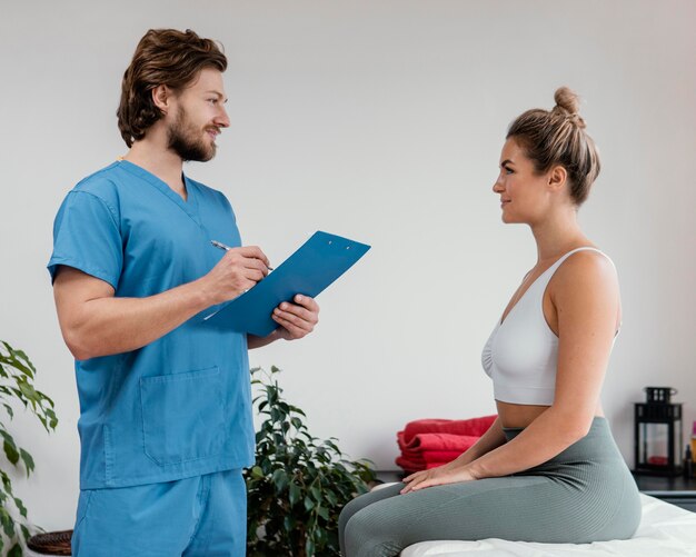 side view of male osteopathic therapist with female patient signing clipboard at the clinic
