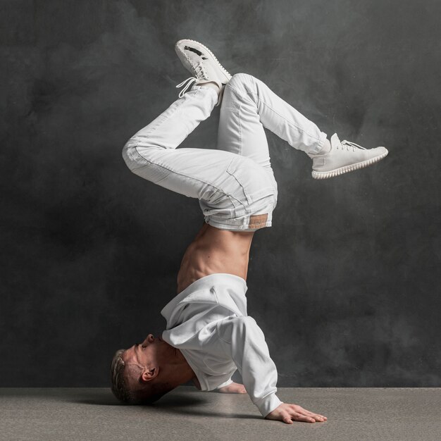 Side view of male performer in jeans and sneakers holding legs up