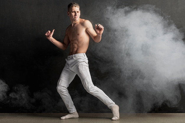 Free photo side view of male performer posing in jeans with smoke and copy space