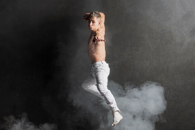 Side view of male performer posing in mid-air with smoke