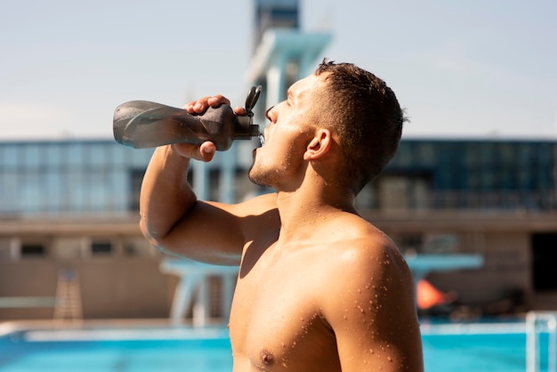 Side view of male swimmer drinking water to stay hydrated