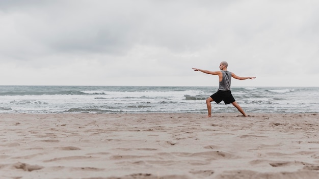 Side view of man on the beach exercising yoga with copy space