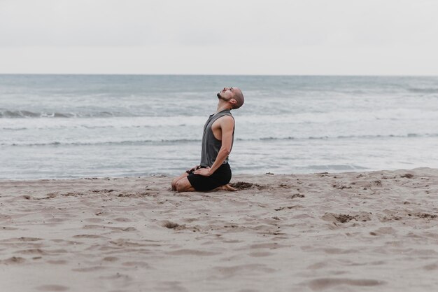 Человек на пляже медитирует, вид сбоку