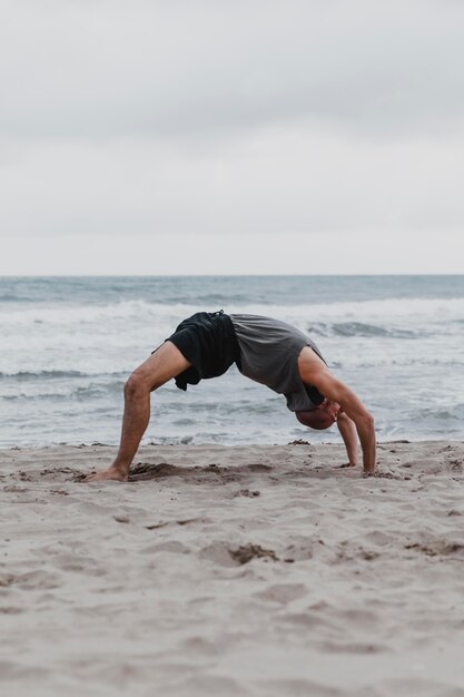 Вид сбоку человека на пляже в позе йоги