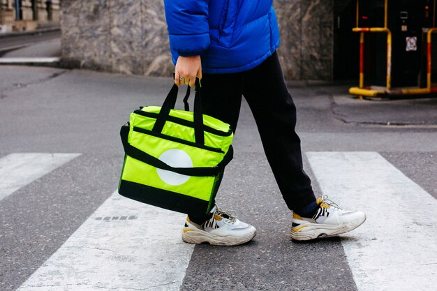 サイドビューの男性が歩行者ゼブラ道のライトグリーンのバッグで注文を運ぶ